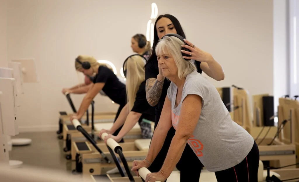 Pregnant woman exercising on a Pilates reformer with an instructor guiding her form in a studio setting