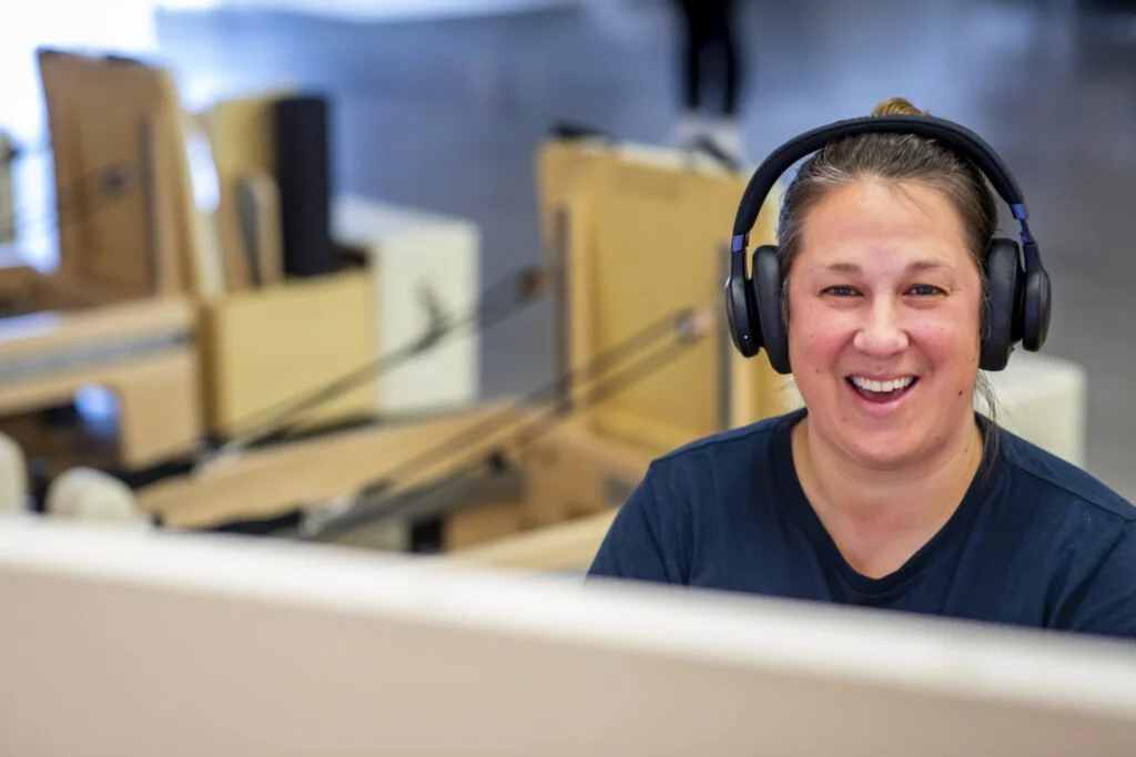 Smiling woman wearing headphones at a Pilates studio with equipment visible in the background
